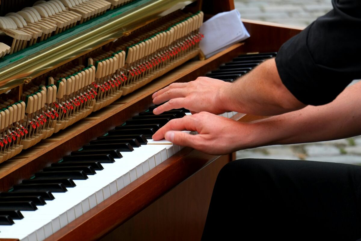 A piano technician's hands tuning an open piano, hammers and strings visible